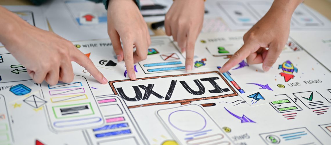 A close-up image of a developer's fingers pointing at UI and UX prototype paper on a table. tech company, startup, user experience design, user interface design