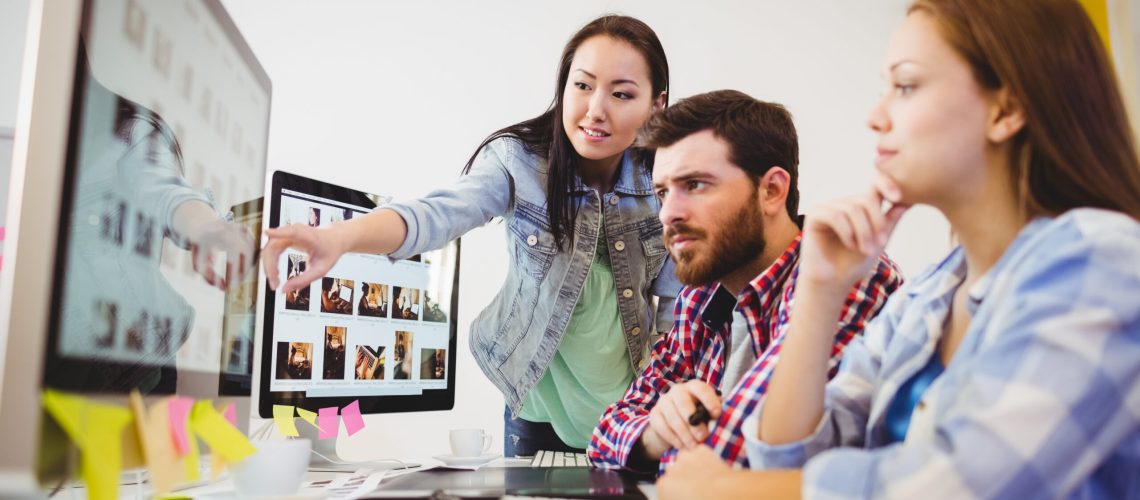 Businesswoman showing computer screen to coworkers in creative office