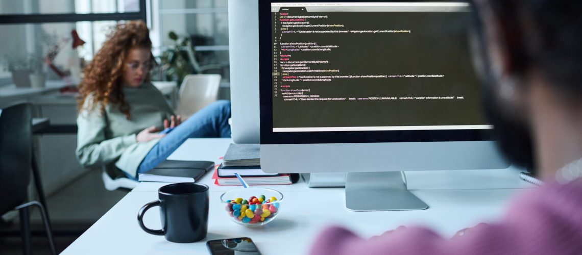 Rear view of developer working with security codes on computer at his workplace with woman working in background