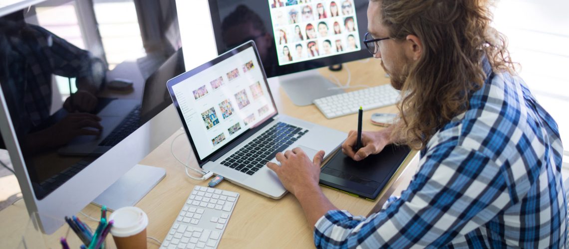 Male executive working over laptop and graphic tablet at his desk in office