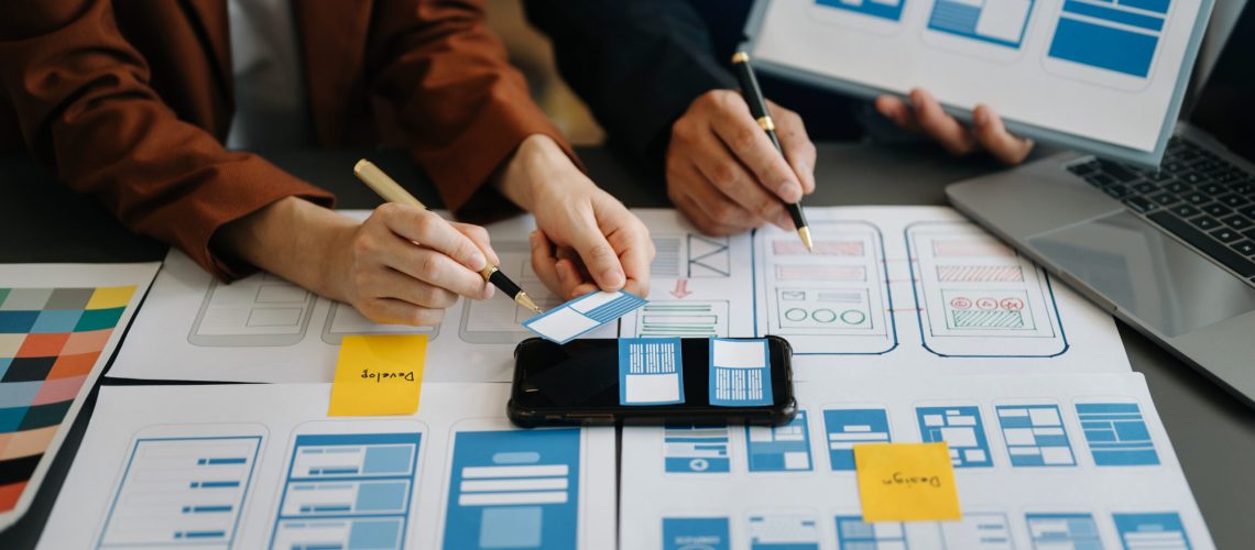 UX developer and ui designer brainstorming about mobile app interface wireframe design with customer breif and color code at modern office.